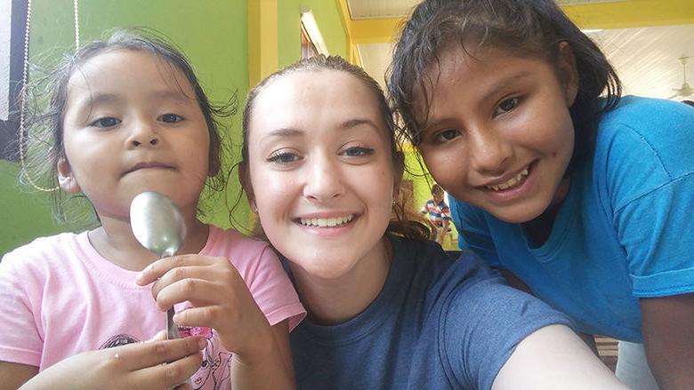 Kelsey Brumbaugh poses with two girls at Andrea’s Home of Hope and Joy in the cafeteria