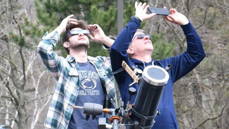 Two people with telescopes looking up at eclipse